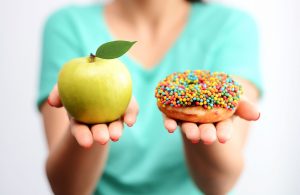 Women holding an apple and a donut demonstrating bad habits vs good habits