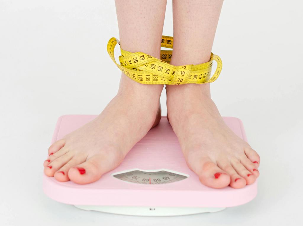 Females feet on a scale wrapped in a tape measure 